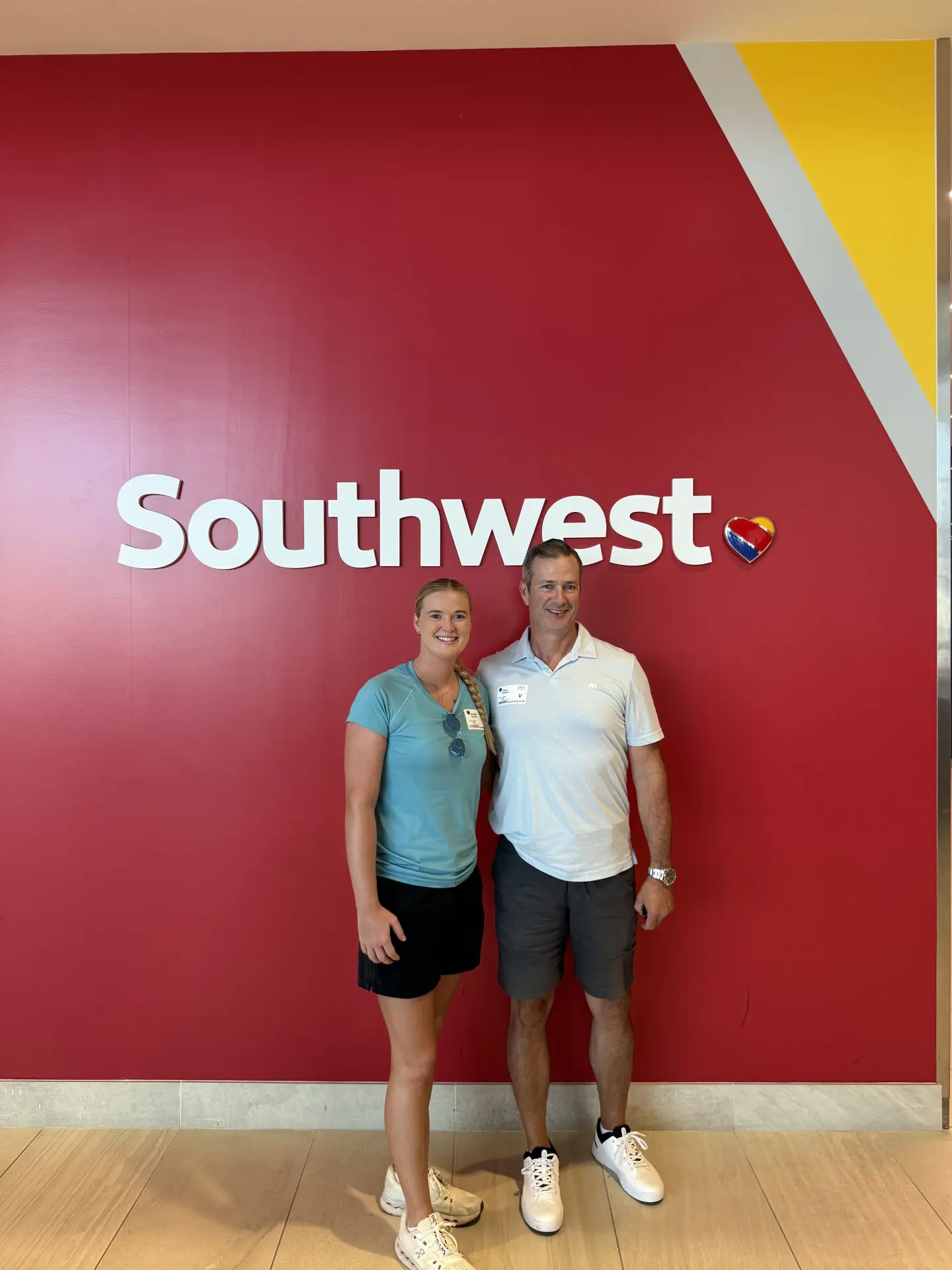 Two smiling visitors wearing badges posing in front of a red Southwest Airlines logo wall